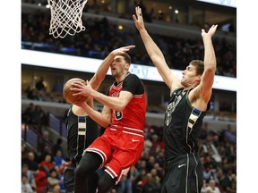 Chicago Bulls guard Zach LaVine (8) gets a hand in the face by Milwaukee Bucks forward Nikola Mirotic on his way to the basket during the first half of an NBA basketball game Monday, Feb. 25, 2019, in Chicago. on the right is Milwaukee Bucks center Brook Lopez.