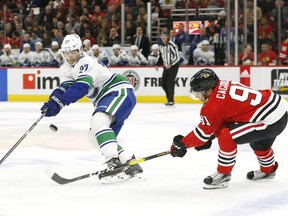 Vancouver Canucks defenseman Ben Hutton (27) and Chicago Blackhawks center Drake Caggiula (91) chase a loose puck during the first period of an NHL hockey game Thursday, Feb. 7, 2019, in Chicago.