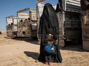 A woman stands with her child near the transport trucks Tuesday.