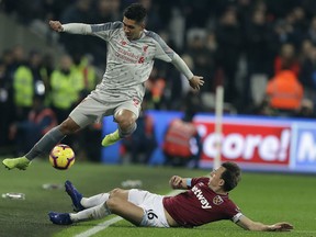 Liverpool's Roberto Firmino, left, and West Ham's Mark Noble challenge for the ball during the English Premier League soccer match between West Ham United and Liverpool at the London Stadium in London, Monday, Feb. 4, 2019.