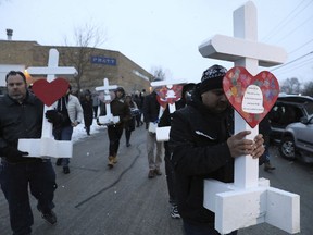 Casildo Cuevas, right, holds a victim's cross as he walks to the Aurora police station after a makeshift memorial Sunday, Feb. 17, 2019, in Aurora, Ill., near Henry Pratt Co. manufacturing company where several were killed on Friday. Authorities say an initial background check five years ago failed to flag an out-of-state felony conviction that would have prevented a man from buying the gun he used in the mass shooting in Aurora.