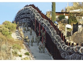 In this Saturday, Feb. 2, 2019 photo, U.S. Army troops place additional concertina wire to the border fence on a hillside above Nelson Street in downtown Nogales, Ariz. Nogales, Mexico is seen at right. The small Arizona border city is fighting back against the installation of razor fencing that now covers the entirety of a tall border fence along the city's downtown area. The city of Nogales, which sits on the border with Nogales, Mexico, is contemplating a proclamation Wednesday, Feb. 6, 2019, condemning the use of concertina wire in its town.