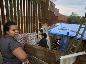 FILE - In this Jan. 16, 2019, file photo, Yuli Arias, left, stands near a newly-replaced section of the border wall as her mother, Esther Arias, center, stands in the family's house that was once threatened by construction along the border in Tijuana, Mexico. The Trump administration said Thursday, Feb. 7, 2019, it would waive environmental reviews to replace up to 14 miles (22.5 kilometers) of border barrier in San Diego, shielding itself from potentially crippling delays.