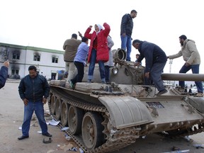 FILE - In this Feb. 21, 2011 file photo, people stand on a tank inside a security forces compound in the eastern Libyan city of Benghazi. Libyans are celebrating the eighth anniversary of their 2011 uprising that led to the overthrow and killing of longtime dictator Moammar Gadhafi, although the intensity of the festivities is underlining the split between the country's east and west. Hundreds of people reveled Sunday in the western cities of Tripoli, Misrata and Zawiya, where bands played and flags lined the streets.