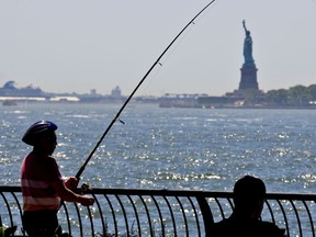 FI LE - In this June 17, 2018, file photo, man fishes from the Battery City Park esplanade as temperature edge near 90 degrees in New York. The weather in New York City in a few decades will feel like how Arkansas is now. Chicago will seem like Kansas City and San Francisco will get a Southern California climate if global warming pollution continues at the current pace, a new study finds.