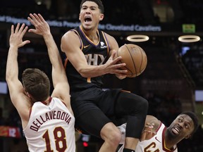 Phoenix Suns' Devin Booker, center, drives to the basket between Cleveland Cavaliers' Matthew Dellavedova, left, and David Nwaba in the second half of an NBA basketball game, Thursday, Feb. 21, 2019, in Cleveland.