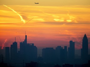 A plane flies over the banking district during sunrise in Frankfurt, Germany, Saturday, Feb. 16, 2019.