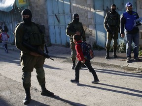 In this Tuesday, Feb. 12, 2019 photo, A Palestinian observers, right, watches as children walk past Israeli soldiers on their way to school in the West Bank city of Hebron. Following Israel's expulsion of an international observer force from this volatile West Bank city, Palestinian activists are trying to fill the void by launching their own patrols to document alleged Israeli settler violence.