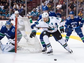 San Jose Sharks' Joe Pavelski (8) is checked by Vancouver Canucks' Ben Hutton (27) as he skates with the puck behind Vancouver Canucks goalie Michael DiPietro, left, during the third period of an NHL hockey game in Vancouver, on Monday February 11, 2019.
