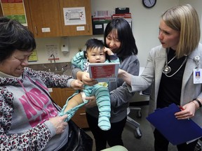 CORRECTS SPELLING OF ABEL, NOT ABLE - As his mother Wenyi Zhang holds him, one-year-old Abel Zhang looks at the book being given him by Dr. Lauren Lawler, right, as his grandmother Ding Hong helps with his clothes moments after the child received the last of three inoculations, including a vaccine for measles, mumps, and rubella (MMR), at the International Community Health Services Wednesday, Feb. 13, 2019, in Seattle. A recent measles outbreak has sickened dozens of people in the Pacific Northwest, most in Washington state and, of those, most are concentrated in Clark County, just north of Portland, Oregon. Washington Gov. Jay Inslee declared a state of emergency over the outbreak last month.
