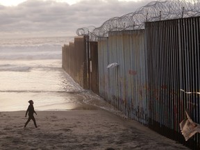 FILE - In this Jan. 9, 2019 file photo, a woman walks on the beach next to the border wall topped with razor wire in Tijuana, Mexico. Congressional negotiators reached agreement to prevent a government shutdown and finance construction of new barriers along the U.S.-Mexico border, overcoming a late-stage hang-up over immigration enforcement issues that had threatened to scuttle the talks.