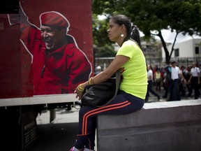 A supporter of Venezuela's President Nicolas Maduro sits next to an image depicting the late president Hugo Chavez during an "anti-intervention" march coinciding with the anniversary of the deadly 1989 social uprising against neoliberal measures known as the Caracazo, in Caracas, Venezuela, Wednesday, Feb. 27, 2019.