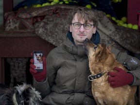 In this photo taken on Saturday, Feb. 2, 2019, Vaidas Gecevicius, who developed an app helping to match stray dogs with potential owners, poses for a picture with a dog and shows this dog's profile on the app in Vilnius, Lithuania.  A group of enthusiasts have launched an app that helps match aspiring dog owners with stray dogs.