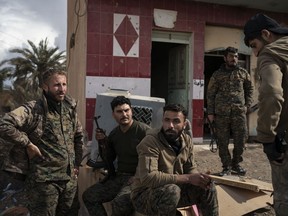 U.S.-backed Syrian Democratic Forces (SDF) fighters stand outside a building used as a temporary base near the last land still held by Islamic State militants in Baghouz, Syria, Monday, Feb. 18, 2019. Hundreds of Islamic State militants are surrounded in a tiny area in eastern Syria are refusing to surrender and are trying to negotiate an exit, Syrian activists and a person close to the negotiations said Monday.
