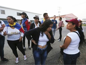 Youths wearing white T-shirts and draped Venezuelan flags over their shoulders wait for permission to cross through an unmarked trail between high bushes to sneak into Colombia for the "Venezuela Aid Live" concert, in Palotal, Venezuela, Friday, Feb. 22, 2019. Venezuela's power struggle is set to become a battle of the bands Friday when musicians demanding President Nicolas Maduro allow in humanitarian aid and those supporting his refusal sing in rival concerts being held at both sides of a border bridge where tons of donated food and medicine are stored.
