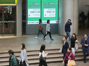 People walk past an electronic board showing Hong Kong share index outside a bank in Hong Kong, Thursday, Feb. 28, 2019. Asian shares are mixed as investors fret over the status of China-U.S. trade talks after U.S. benchmarks closed mostly lower.