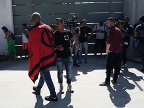 Friends, fans and journalists stand at the entrance of the Flamengo soccer training center as they wait for information after a fire in the facilities of the soccer club in Rio de Janeiro, Brazil, Friday, Feb. 8, 2019. Firefighters say a number of people have died in an early morning fire at a training facility of one Brazil's largest soccer clubs..