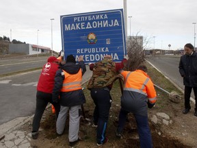 Workers remove a road sign that reads ''Republic of Macedonia'' in the southern border with Greece, near Gevgelija, Wednesday, Feb. 13, 2019. The small Balkan country of Macedonia officially changed its name Tuesday by adding a geographic designation that ends a decades-old dispute with neighboring Greece and secures its entry into NATO.
