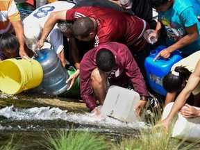 People collect water from a broken pipe, flowing into a sewage canal at the Guaire river in Caracas on March 11, 2019, as a massive power outage continues affecting some areas of the country.