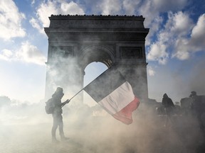 A protester holds a French national flag as he walks among tear gas smoke past the Arc de Triomphe in Paris.