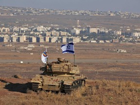 A file photo taken on October 18, 2017 shows an Israeli flag fluttering above the wreckage of an Israeli tank sitting on a hill in the Israeli-occupied sector of the Golan Heights and overlooking the border with Syria.
