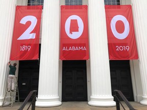 In this Feb. 28, 2019, photo a worker adjusts a banner celebrating Alabama's bicentennial outside the Department of Archives and History in Montgomery, Ala. Alabama is the latest state trying to balance a painful past with other parts of its history as it recognizes its 200th birthday as a state.