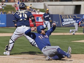 Texas Rangers' Nolan Fontana scores behind Milwaukee Brewers catcher Yasmani Grandal on a sacrifice fly by Willie Calhoun in the sixth inning of a spring training baseball game Tuesday, March 19, 2019, in Phoenix