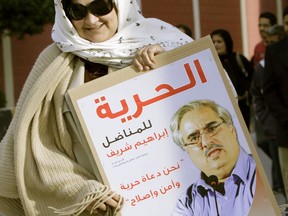 FILE - In this Feb. 22, 2012 file photo, Fareeda Ghulam, the wife of Bahrain opposition politician Ebrahim Sharif, carries a poster with her husband's image as she arrives for an anti-government rally outside the offices of the United Nations in Manama, Bahrain. Activists said Wednesday, March 13, 2019, that Sharif now faces up to six months in prison for a tweet about Sudanese President Omar al-Bashir. Poster reads, "Freedom for Ebrahim Sharif. We are the voices of freedom, peace and reform."