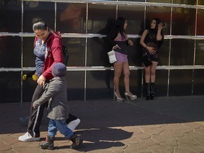 In this March 5, 2019, image, Ruth Aracely Monroy walks with her sons as they pass two women in the red-light district of Tijuana, Mexico.