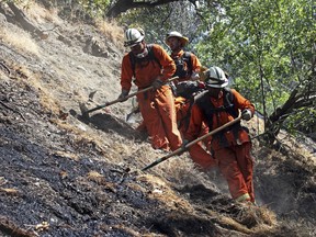 FILE - In this June 12, 2018 file photo, firefighters clear burned and unburned brush from a hillside above Portola Drive after a wildfire broke out in the Benedict Canyon area of Los Angeles. California is calling in the National Guard for the first time to help protect communities from wildfires like the one that destroyed much of the city of Paradise last fall. Starting in April 2019, 110 California National Guard troops will receive 11 days of training in using shovels, rakes and chain saws to thin trees and brush.