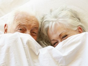 Old couple mischievously peek out from between white sheets.