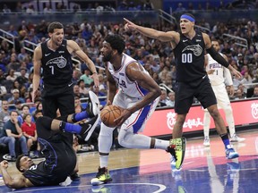 Philadelphia 76ers' Joel Embiid, center, is called for a charge as he runs into Orlando Magic's Khem Birch, lower left, as Magic's Michael Carter-Williams (7) and Aaron Gordon (00) look on during the first half of an NBA basketball game, Monday, March 25, 2019, in Orlando, Fla.