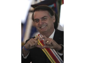 Brazil's President Jair Bolsonaro flashes a heart-hand signal after he was presented with the Order of Military Judicial Merit, in Brasilia, Brazil, Thursday, March 28, 2019. Bolsonaro, a former army captain who waxes nostalgic for the 1964-1985 dictatorship, on Monday asked Brazil's Defense Ministry to organize "due commemorations" to mark the upcoming March 31st anniversary of Brazil's 1964 military coup.