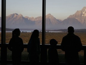 FILE - In this Aug. 28, 2016 file photo visitors watch the morning sun illuminate the Grand Tetons from within the Great Room at the Jackson Lake Lodge, in Grand Teton National Park, north of Jackson Hole, Wyo. Grand Teton National Park in western Wyoming seeks thoughts from the public on plans for a new network of cell towers amid questions about how the National Park Service balances public safety with the experience of wilderness. The park currently has two cell towers as part of a system built piecemeal-fashion, with some fiber-optic lines buried without conduit and poorly mapped.