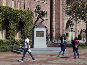FILE - In this March 12, 2019 file photo, people pose for photos in front of the iconic Tommy Trojan statue on the campus of the University of Southern California in Los Angeles. The past year has been a bruising one for the Los Angeles university. The president who helped boost the school's endowment above $6 billion had to step down amid investigations into a medical school dean accused of smoking methamphetamine with a prostitute who overdosed, its longtime gynecologist was accused of sexual misconduct by hundreds of women he examined over decades and an assistant men's basketball coach pleaded guilty to charges stemming from an FBI probe of corruption in college basketball.