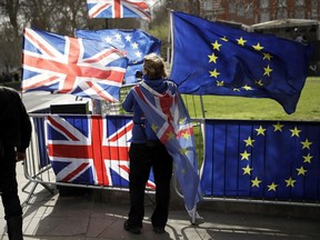 An anti-Brexit supporter stands by European and British Union flags placed opposite the Houses of Parliament in London, Monday, March 18, 2019. British Prime Minister Theresa May was making a last-minute push Monday to win support for her European Union divorce deal, warning opponents that failure to approve it would mean a long -- and possibly indefinite -- delay to Brexit. Parliament has rejected the agreement twice, but May aims to try a third time this week if she can persuade enough lawmakers to change their minds.
