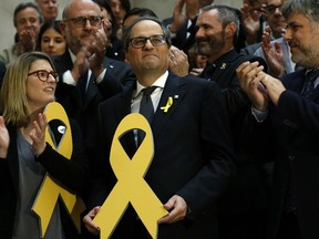 FILE - In this Monday, May 14, 2018 file photo, newly appointed Catalan president Quim Torra, center, holds a yellow ribbon in support of Catalonian politicians who have been jailed on charges of sedition, at the end of a parliamentary vote session in Barcelona, Spain. Prosecutors in Spain said in a statement Wednesday March 27, 2019, they are bringing charges of disobedience against Catalan regional president Quim Torra after he allegedly failed to comply with orders from the country's electoral board.