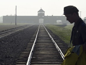 FILE - In this file photo dated Friday, July 29, 2016, a man crosses the iconic rails leading to the former Nazi death camp of Auschwitz-Birkenau in Poland.  Police official Malgorzata Jurecka in Poland said Sunday March 31, 2019, an American visitor to the former Auschwitz-Birkenau death camp attempted to steal a metal part of the rail tracks where prisoners were unloaded, and he has been charged with attempted theft.