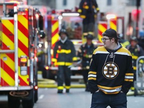 A Boston Bruins fan heads to an NHL hockey game between the Bruins and the Ottawa Senators at TD Garden while firefighters battle a three-alarm blaze in an adjacent building under construction in Boston, Saturday, March 9, 2019.