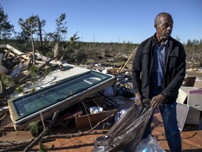 FILE- In this March 5, 2019 file photo, Richard Tate retrieves personal items from what's left of his home where he survived a tornado with his wife in Beauregard, Ala.  The town of Beauregard worked for months without success to build a storm shelter before the twister struck.