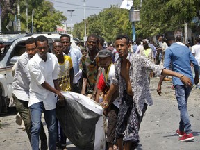 Somalis carry away a man who was wounded after blast outside a restaurant in Mogadishu, Somalia,  Thursday, March 28, 2019. A Somali police officer says an explosives-laden vehicle has detonated outside a restaurant in Somalia's capital, Mogadishu.