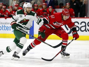 Minnesota Wild's Jason Zucker (16) chips the puck ahead of Carolina Hurricanes' Trevor van Riemsdyk (57) during the first period of an NHL hockey game, Saturday, March 23, 2019, in Raleigh, N.C.
