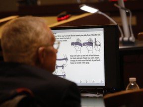 Former U.S. Sen. Harry Reid sits in front of a monitor showing instructions for an exercise band in court Tuesday, March 26, 2019, in Las Vegas. A jury in Nevada heard opening arguments Tuesday in Reid's lawsuit against the maker of a flexible exercise band that he says slipped from his hand while he used it in January 2015, causing him to fall and suffer lasting injuries including blindness in one eye.