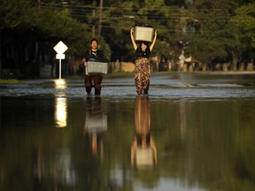 FILE - In this Monday, Sept. 4, 2017 file photo, Mariko Shimmi, right, helps carry items out of the home of Ken Tani in a neighborhood still flooded from Harvey in Houston. Some neighborhoods around Houston remain flooded and thousands of people have been displaced by torrential rains and catastrophic flooding since Harvey slammed into Southeast Texas last week. According to a scientific report from the United Nations released on Wednesday, March 13, 2019, climate change, a global major extinction of animals and plants, a human population soaring toward 10 billion, degraded land, polluted air, and plastics, pesticides and hormone-changing chemicals in the water are making the planet an increasing unhealthy place for people.