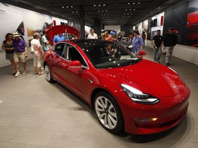 FILE- In this July 6, 2018, file photo, prospective customers confer with sales associates as a Model 3 sits on display in a Tesla showroom in the Cherry Creek Mall in Denver. Tesla is suffering one of its worst sell-offs of the year after announcing it would begin closing all of its stores in favor of selling its electric cars exclusively online. The goal is to allow Tesla to lower the price of its Model 3, the vehicle that CEO Elon Musk envisions as the company's first mass-market vehicle.