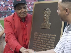 FILE - In this April 20, 2004, file photo, former Cincinnati Reds player Chuck Harmon, left, reaches across a plaque honoring him to shake hands with his son, Chuck Harmon Jr., during ceremonies before the Reds game against the Atlanta Braves in Cincinnati.  Harmon, the Reds' first African-American player, died Tuesday, March 19, 2019. He was 94.