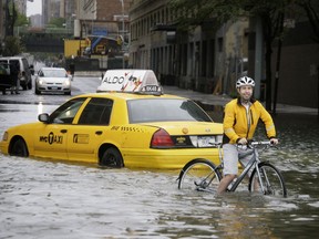 FILE - In this Aug. 28, 2011 file photo, a bicyclist makes his way past a stranded taxi on a flooded New York City street as Tropical Storm Irene passes through the city. Mayor Bill de Blasio is announcing a plan, Thursday, March 14, 2019, to protect lower Manhattan from rising sea levels by surrounding it with earthen berms and extending its shoreline by as much as 500 feet.