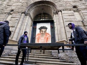 Farooq Al-Said, left, Jasiri X, center, and Jarrion Manning, right, hold a memorial display with a drawing of Antwon Rose II in front of the court house on the first day of the trial for Michael Rosfeld, a former police officer in East Pittsburgh, Pa., begins on Tuesday, March 19, 2019, in Pittsburgh. Rosfeld is charged with criminal homicide in the fatal shooting of Antwon Rose II as he fled during a traffic stop on June 19, 2018.