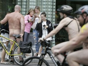 FILE - In this Sept. 8, 2018 file photo, a naked bicyclist poses for photos as other participants ride past during the Philly Naked Bike Ride in Philadelphia. Naked bicyclists say they were so cold riding around Philadelphia last September that this year they'll do it in August. Organizers of the annual Philly Naked Bike Ride say they've "ridden in chilly weather" the last two Septembers so this time they'll saddle up Aug. 24 and "hope it's a scorcher!" The nude ride was on Sept. 8 last year and Sept. 9 the year before that, with temperatures reaching only about 70 degrees Fahrenheit.
