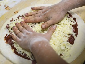 FILE -  In this Sept. 26, 2018 file photo, a worker adds cheese to a raw pizza at a shop in Pittsburgh. A report released Tuesday, March 5, 2019 by the National Academies of Science ties the recommended limit on sodium to a reduced risk of chronic disease. Sodium can be hidden in bread, pizza, soup and an array of other foods.